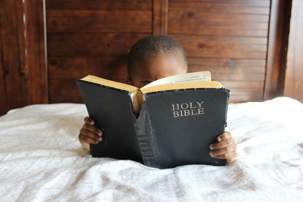 a little boy is stretched out on his stomach, reading a big Bible