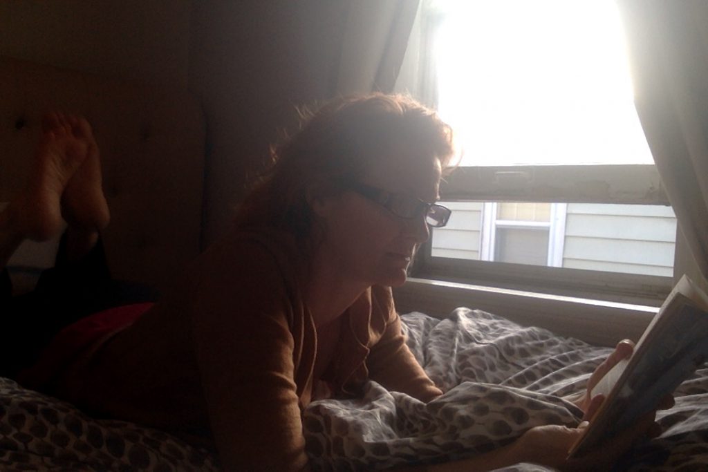 a picture of me, on my stomach on my bed, right next to an open window, reading