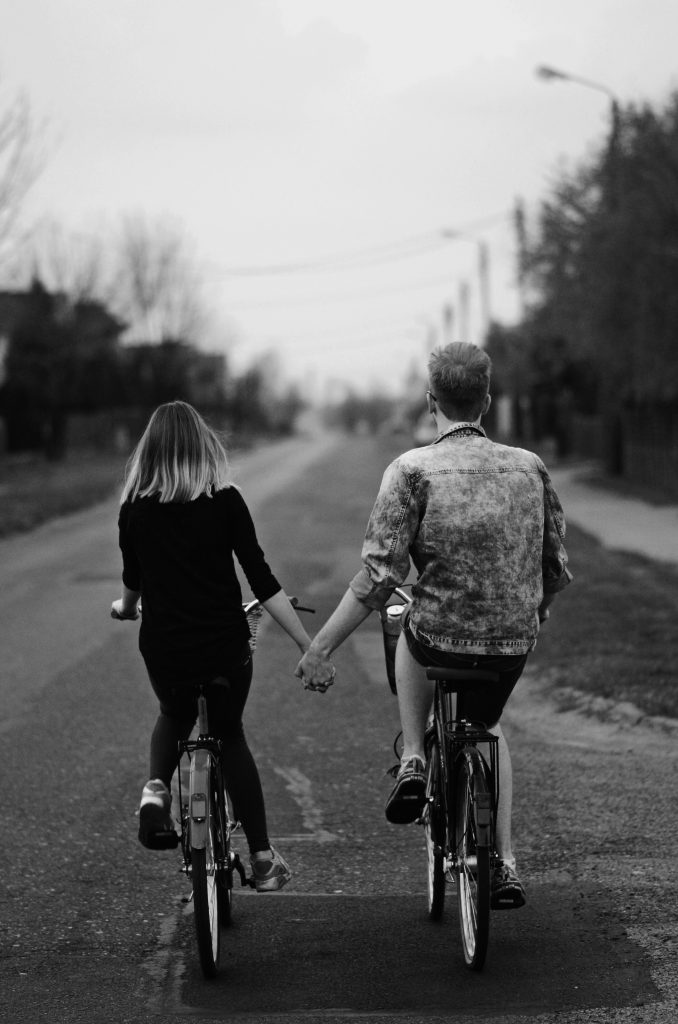 A boy and a girl bicycle up the road while holding hands.