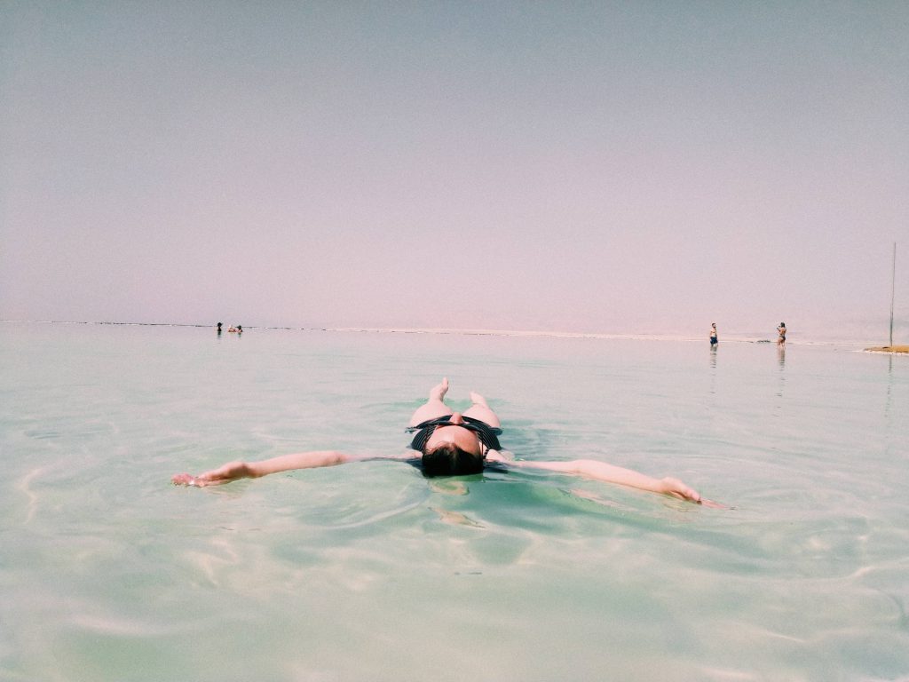 An image of a woman floating on her back in a calm, peaceful sea. Her arms are outstretched.