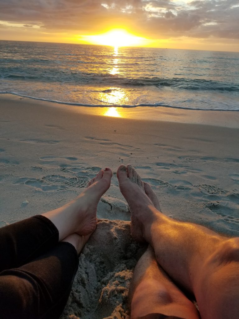 And image of a man and a woman's crossed bare feet on the beach at sunset.