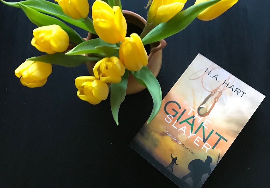 A bouquet of tulips and the book The Giant Slayer on a black table.